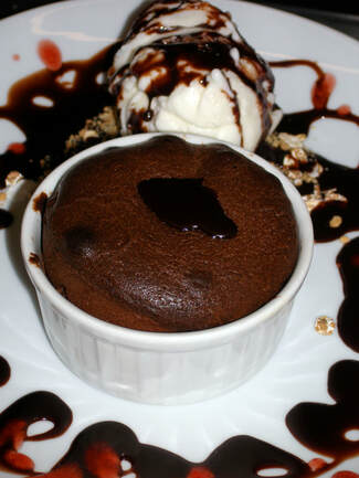 White vanilla ice cream with a brown chocolate drizzle on a plate beside a brown chocolate cake in a bowl beside it.